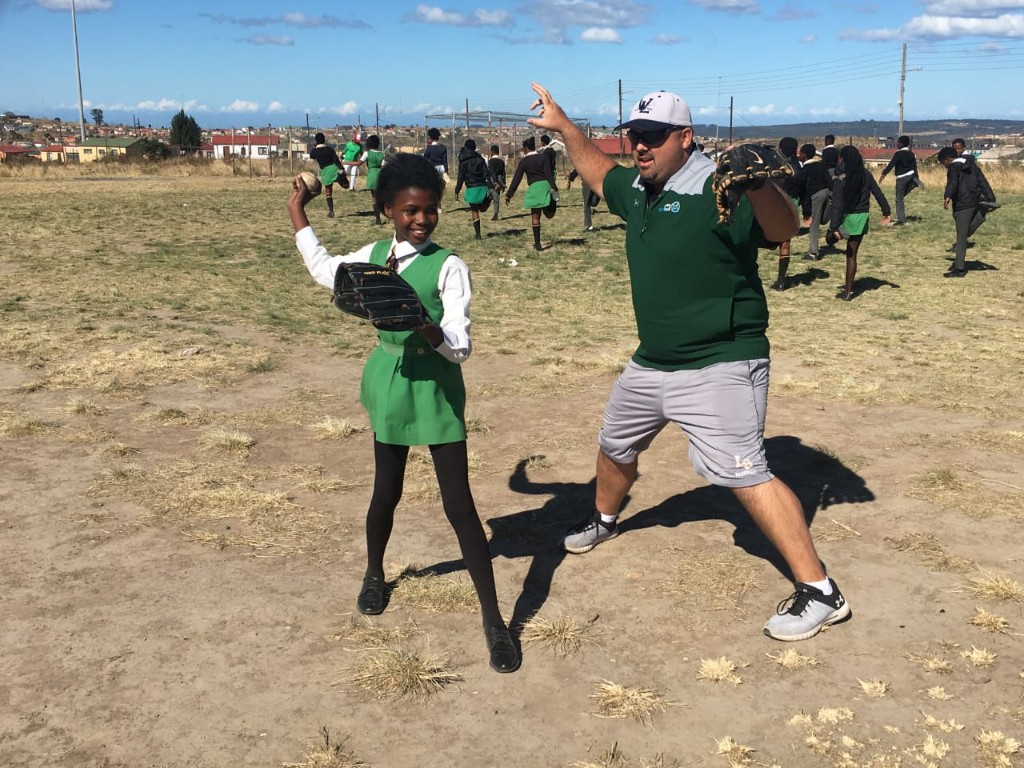 Coach and young girl practicing throwing on baseball field